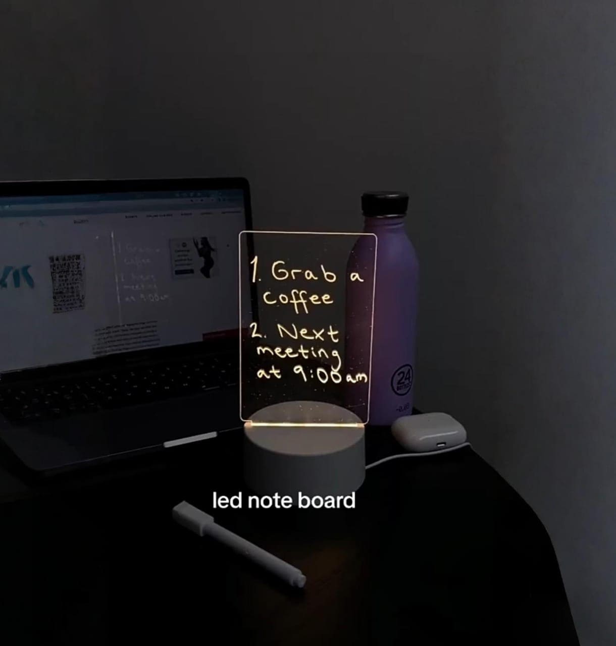LED note board on a desk with a laptop and water bottle in a dimly lit room.